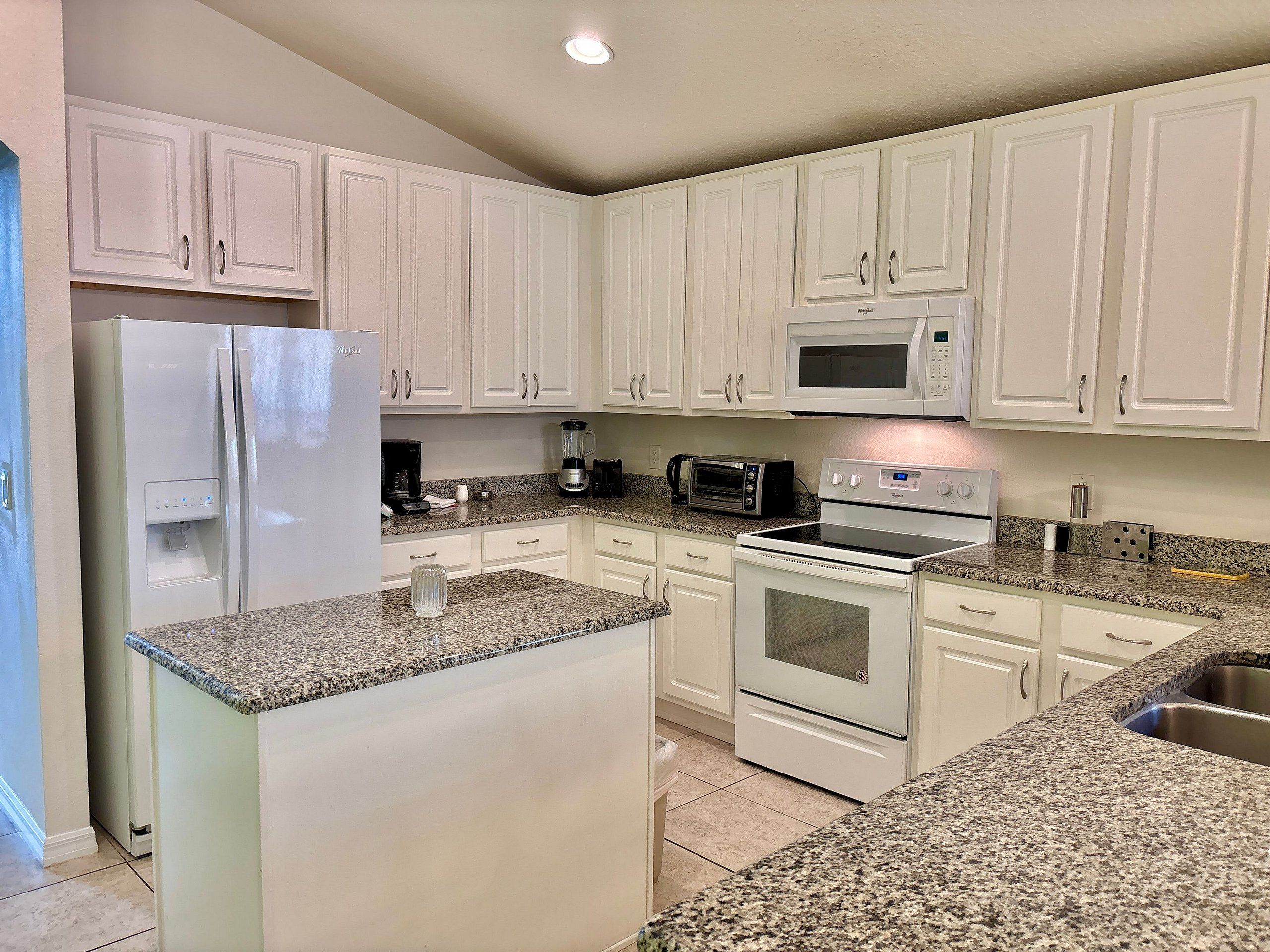 A kitchen with white cabinets, a refrigerator, a microwave, a toaster, and a stove.