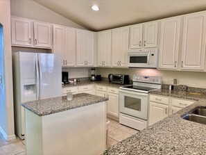 Eine Küche mit weißen Schränken, einem Kühlschrank, einer Mikrowelle, einem Toaster und einem Herd.
