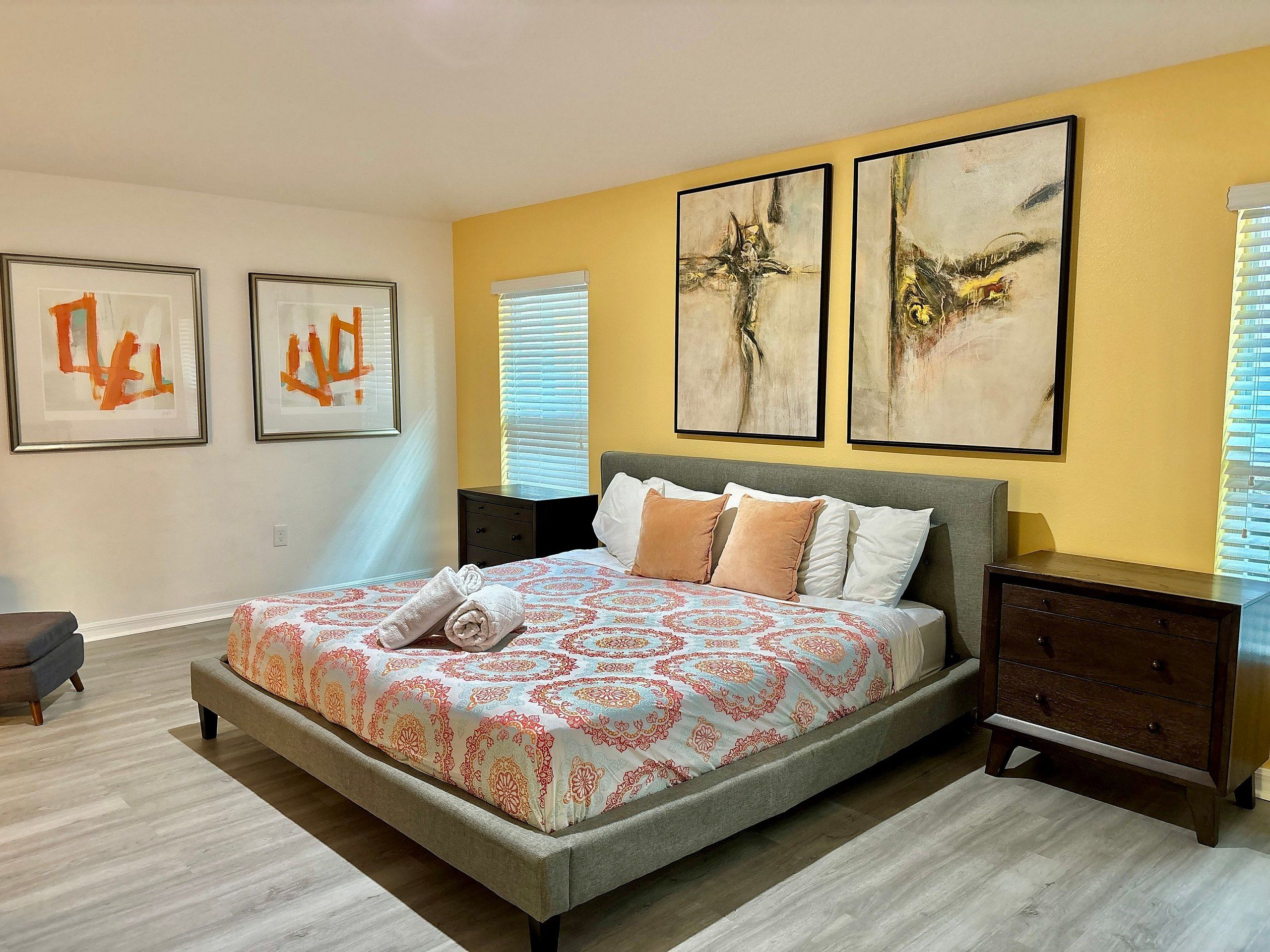 A bedroom with a large bed, two bedside tables, and three abstract paintings on the wall.