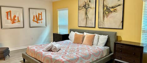 A bedroom with a large bed, two bedside tables, and three abstract paintings on the wall.