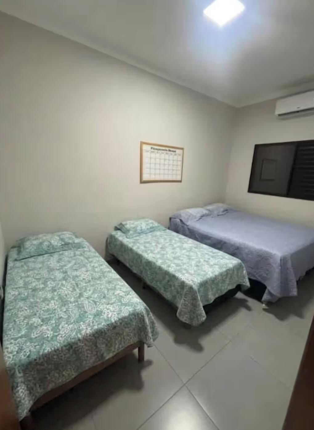 A room with two single beds, a wall calendar, and an air conditioning unit.