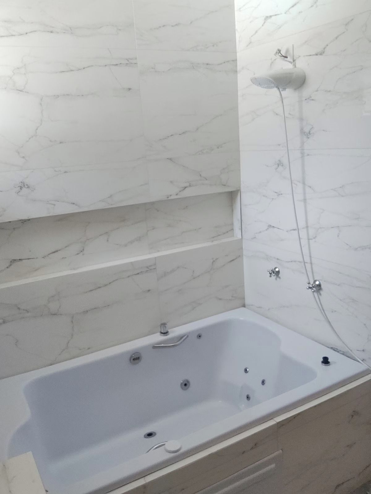 A bathroom with a marble wall, a bathtub, and a shower.