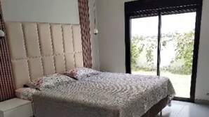 Ein Schlafzimmer mit einem großen Bett, einem Nachttisch und einer Schiebetür zu einem Außenbereich.