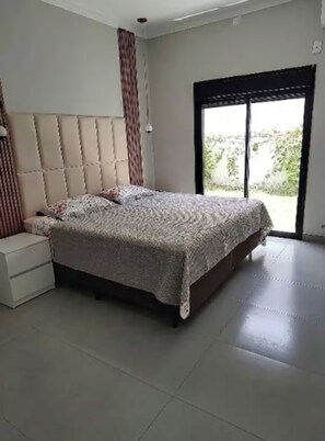 Une chambre avec un grand lit, une table de chevet et une porte-fenêtre coulissante donnant sur un espace extérieur.