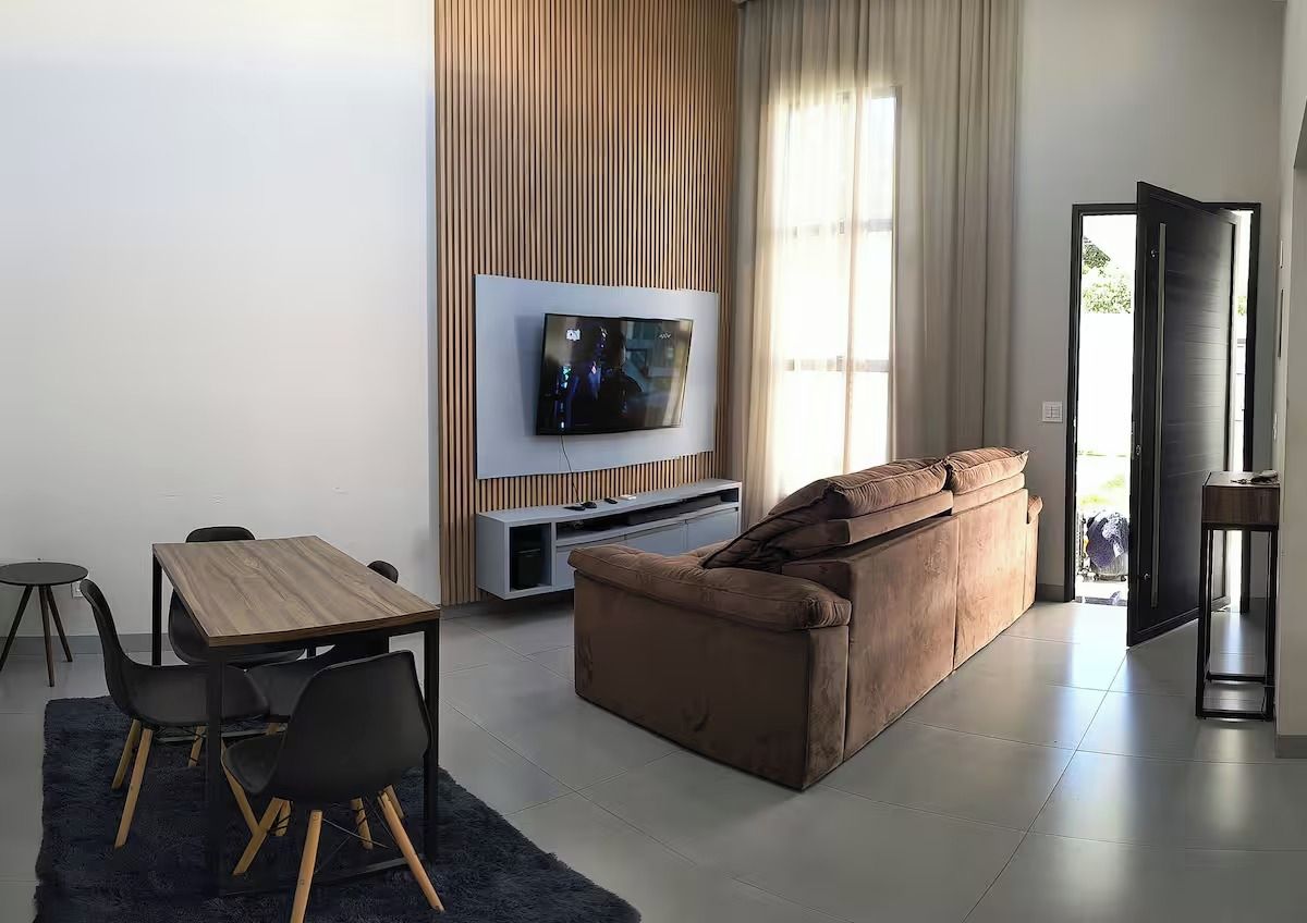 Un salon moderne doté d’un téléviseur à écran plat, d’un canapé marron, d’une table à manger avec des chaises et d’une grande fenêtre agrémentée de rideaux.