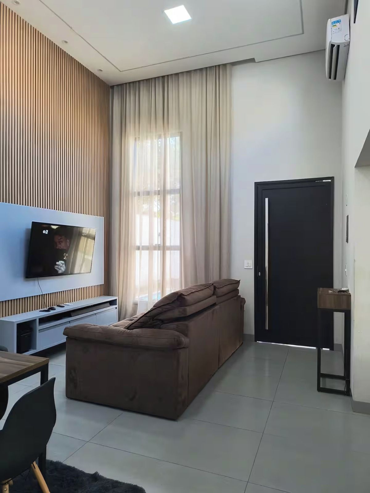 Uma sala de estar moderna com televisão de tela plana, um sofá marrom, parede de destaque em madeira e uma porta preta.