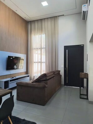 A modern living room with a flat-screen TV, a brown sofa, a wooden accent wall, and a black door.