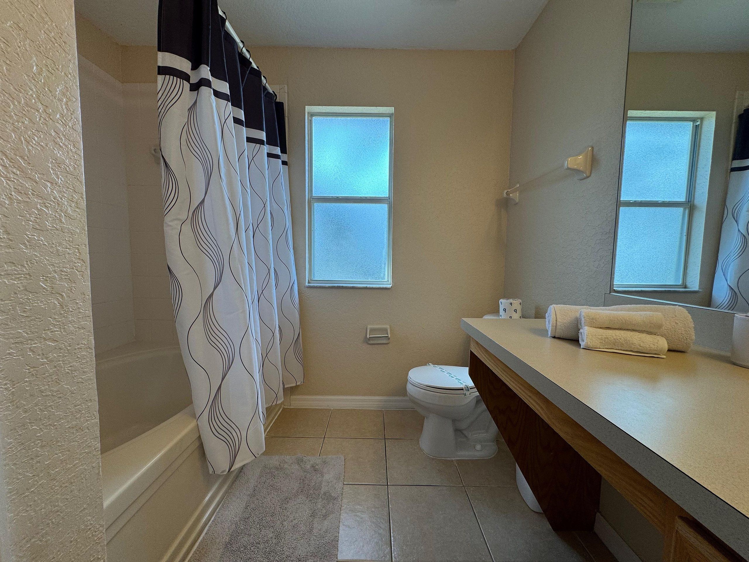 A bathroom with a toilet, a sink with a mirror, a towel, and a shower curtain.