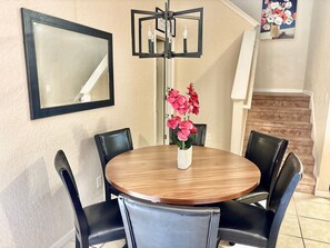 A dining area with a round table, black chairs, a vase with pink flowers, a wall-mounted mirror, and a painting of flowers. - Regal Palms 3BR Home Near Disney With Pool (Davenport)