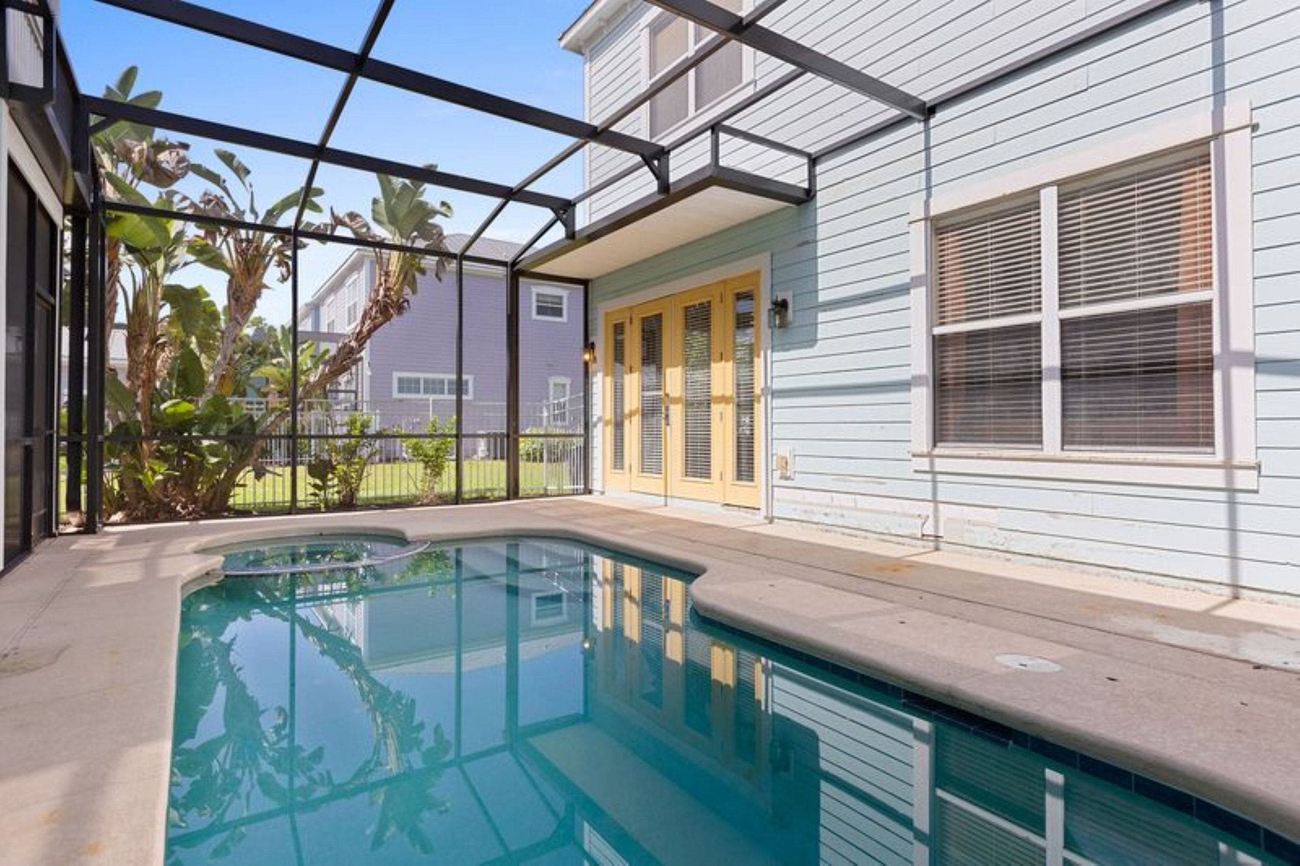 Ein Wohngebiet-Schwimmbad mit überdachter Terrasse, umgeben von Zäunen und Pflanzen.