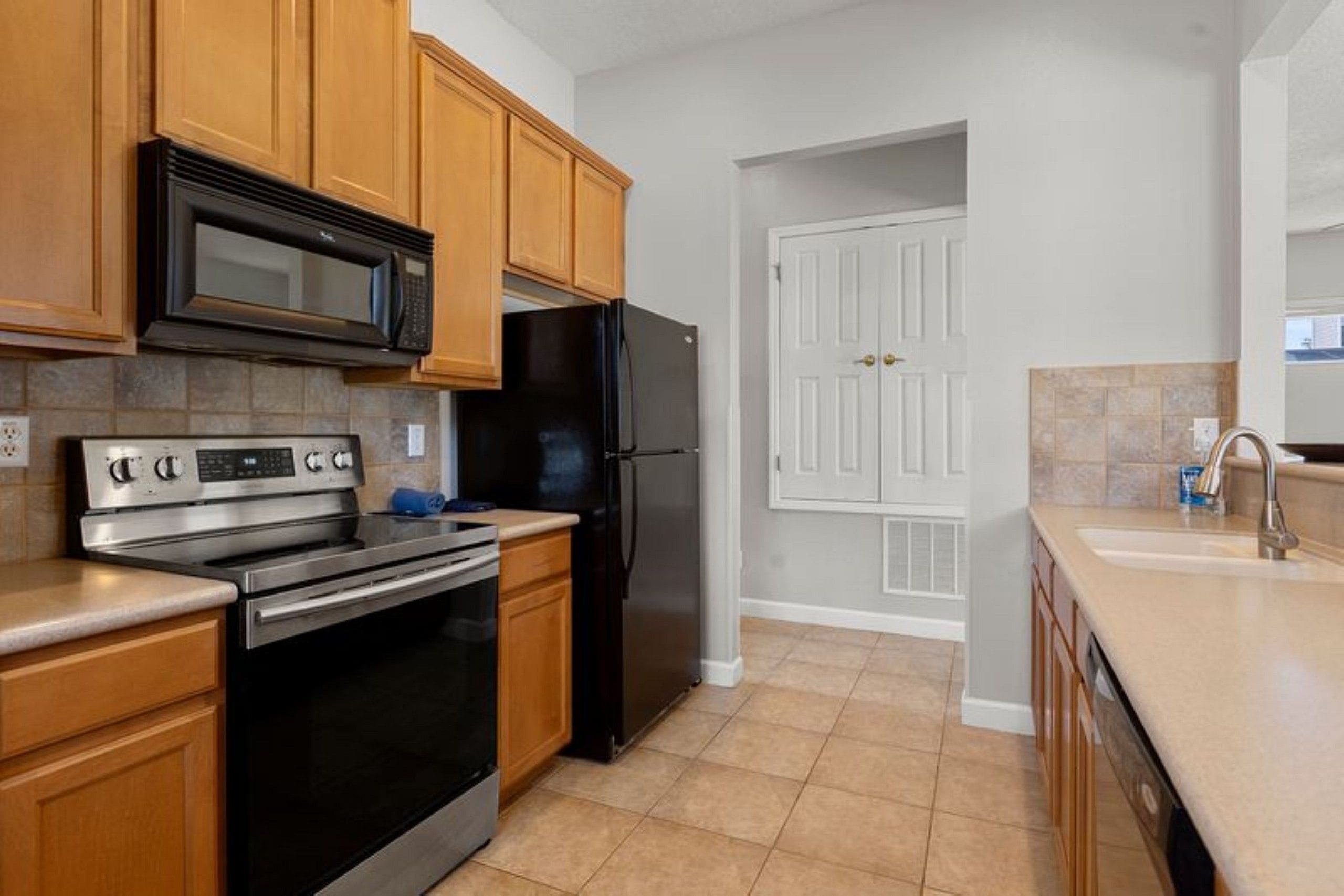 A kitchen with wooden cabinets, a black refrigerator, a stainless steel oven, and a microwave.