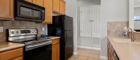 Una cocina con armarios de madera, un refrigerador negro, un horno de acero inoxidable y un microondas.