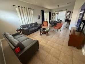 A living room with a sofa, armchair, coffee table, and dining area with chairs and a table. - 4BR Reunion Resort Villa, Pool, Near Disney (Kissimmee)
