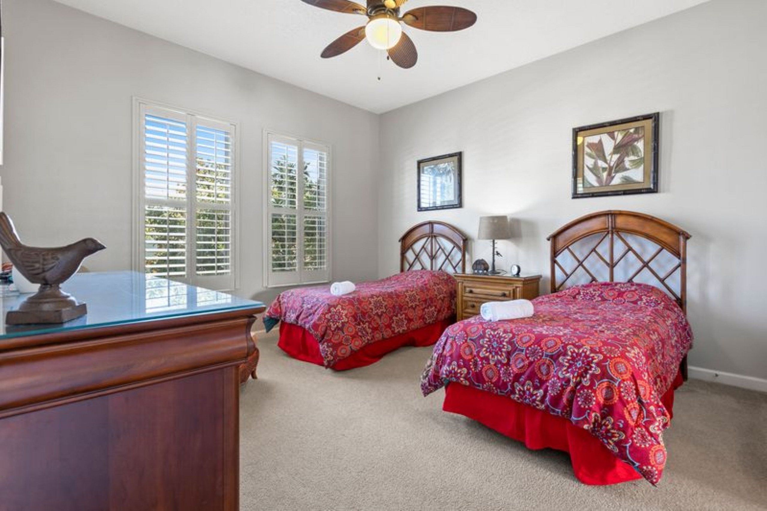 A bedroom with two beds, a desk, a ceiling fan, and a window with blinds.