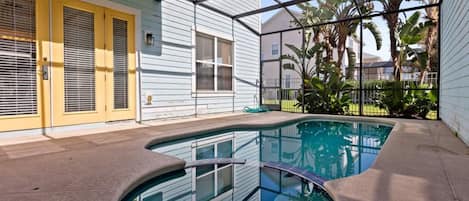 A swimming pool with a curved edge, surrounded by a concrete deck, and adjacent to a building with yellow doors and windows.