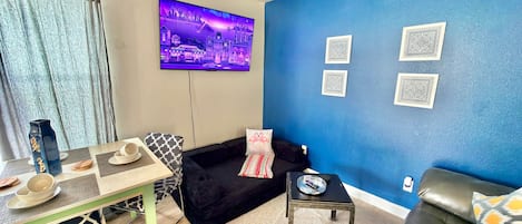 Una sala de estar con televisor, sofá, mesa de centro y pared azul con diseños decorativos.