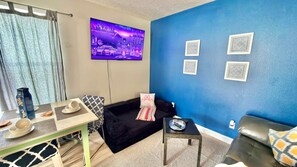 Ein Wohnzimmer mit Fernseher, einer Couch, einem Couchtisch und einer blauen Wand mit dekorativen Mustern.