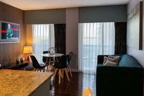 Ein Hotelzimmer mit Essbereich, einer Sitzecke, einem Fernseher und großen Fenstern.