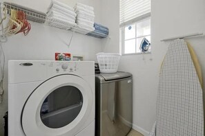 A laundry area with a front-loading washing machine, a drying rack, and a hanging clothes rack. - 5BR Home Near Disney With Pool & Game Room (Kissimmee)