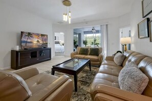 A modern living room with leather sofas, a glass coffee table, and a flat-screen TV. - 5BR Home Near Disney With Pool & Game Room (Kissimmee)