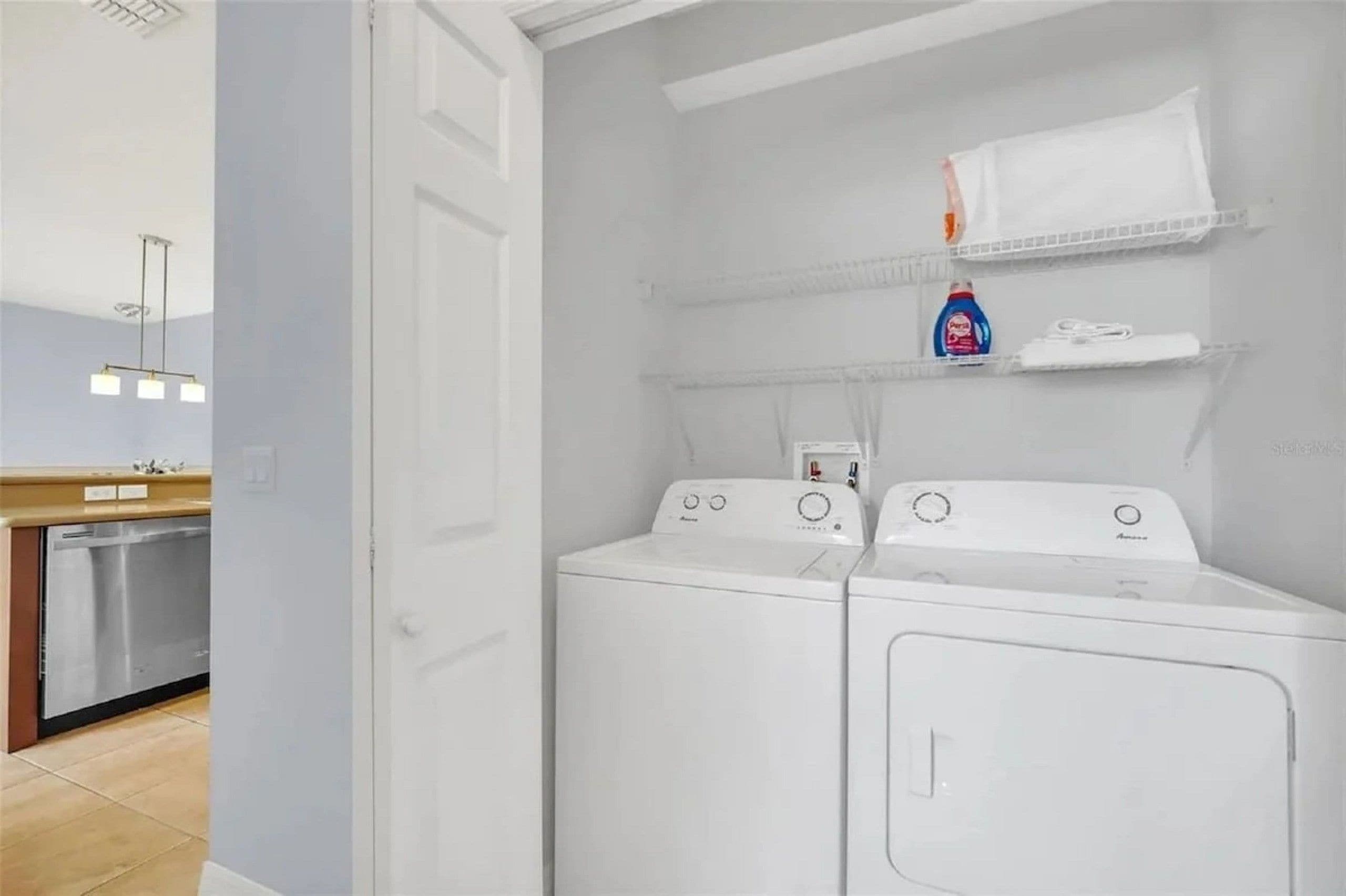 A laundry room with two front-loading washing machines, a shelf with detergent, and a hanging rack.