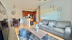 Ein modernes Wohnzimmer mit einem grauen Sofa, einem Couchtisch und einem Essbereich mit einer Küche im Hintergrund.
