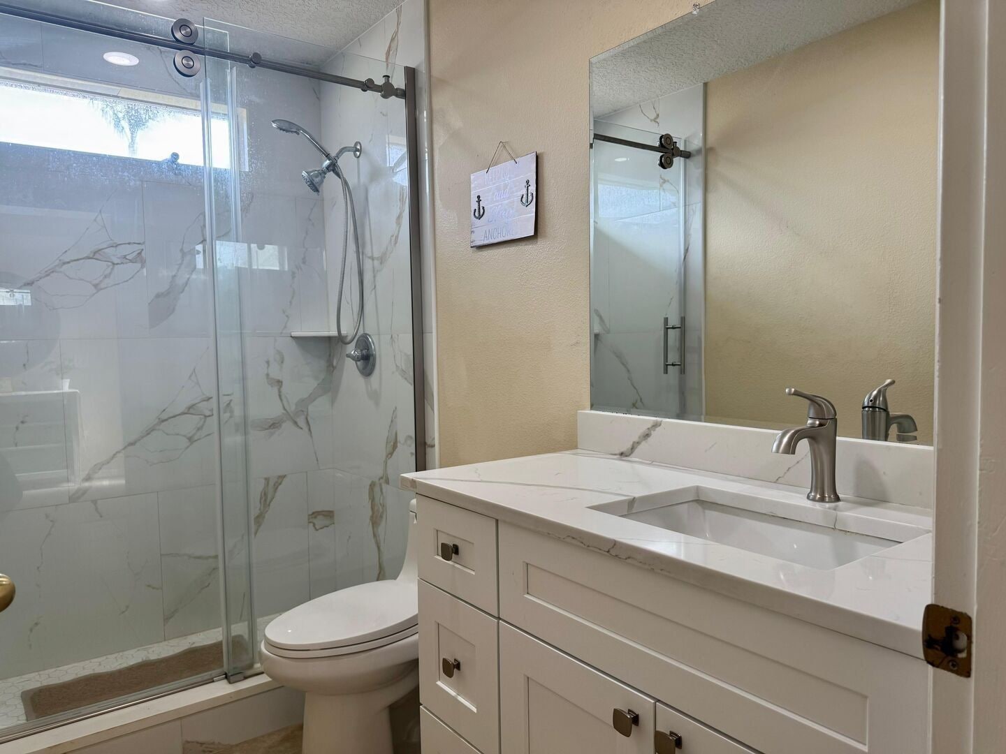 Un baño con ducha envuelta en vidrio, un inodoro, un lavamanos con espejo y paredes con diseño de mármol.