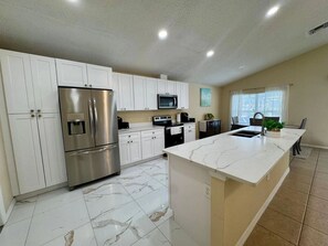 A modern kitchen with white cabinetry, a stainless steel refrigerator, a microwave, and a marble island. - Lake Berkley 3BR Disney 10min, Pool & Lake (Kissimmee)