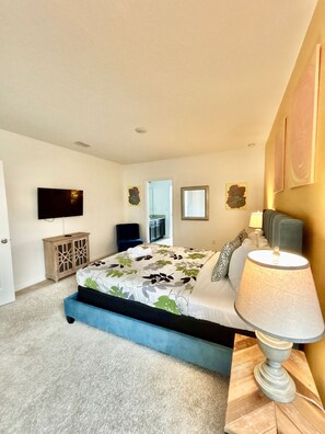 A bedroom with a bed, a bedside lamp, a TV, and a door. - Solterra 7BR Home Pool & Spa Near Disney (Davenport)