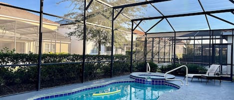 An indoor swimming pool with a glass enclosure, surrounded by lounge chairs and a covered patio area.