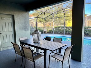 An outdoor patio with a table and chairs, a lantern, and a view of a swimming pool. - 7BR Solterra Home, Pool & spa Near Disney (Davenport)