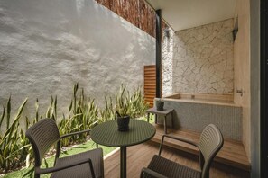 A patio with a round table and chairs, a small potted plant, and a spa area with a bathtub.
