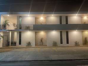 Un bâtiment à deux étages doté de balcons, de plantes en pot et d’une zone d’entrée pavée.