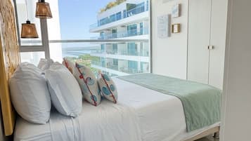 A bedroom with a bed, a window with a view of a building, and a wall with framed items.
