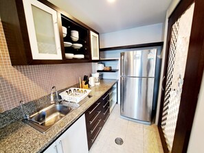 A compact kitchen with a stainless steel refrigerator, a sink with a faucet, and a countertop with various kitchen items. - Luxurious 2-bedroom Condo With Pool View Near BTS Ekkamai Station (Bangkok)