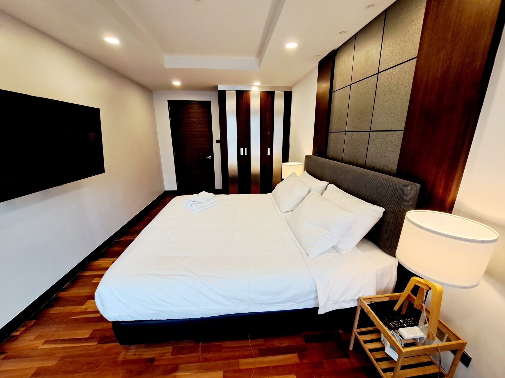 Una camera d'albergo moderna con un letto grande, una TV a schermo piatto fissata al muro e un pavimento in legno.