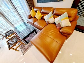 A brown leather sofa with cushions, a glass coffee table, and a patterned rug in a well-lit room with large windows. - Luxurious 2-bedroom Condo With Pool View Near BTS Ekkamai Station (Bangkok)