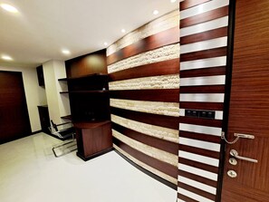 A modern interior with a built-in wooden cabinet, a wall-mounted shelf, and a door with a metal handle. - Luxurious 2-bedroom Condo With Pool View Near BTS Ekkamai Station (Bangkok)