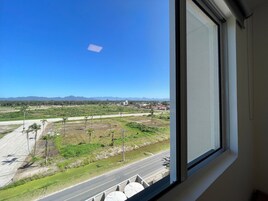 Vista pela janela mostrando uma estrada, céu limpo e montanhas ao longe.