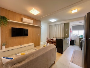 Ein modernes Wohnzimmer mit Flachbildfernseher, einer Couch, einem Essbereich mit Stühlen und einer Küche inklusive Kühlschrank.