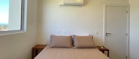 A bedroom with a bed, a window, an air conditioning unit, and a door.
