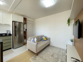 Um espaço de estar moderno com cozinha compacta, sofá com almofadas decorativas, televisão de tela plana e um armário de madeira.