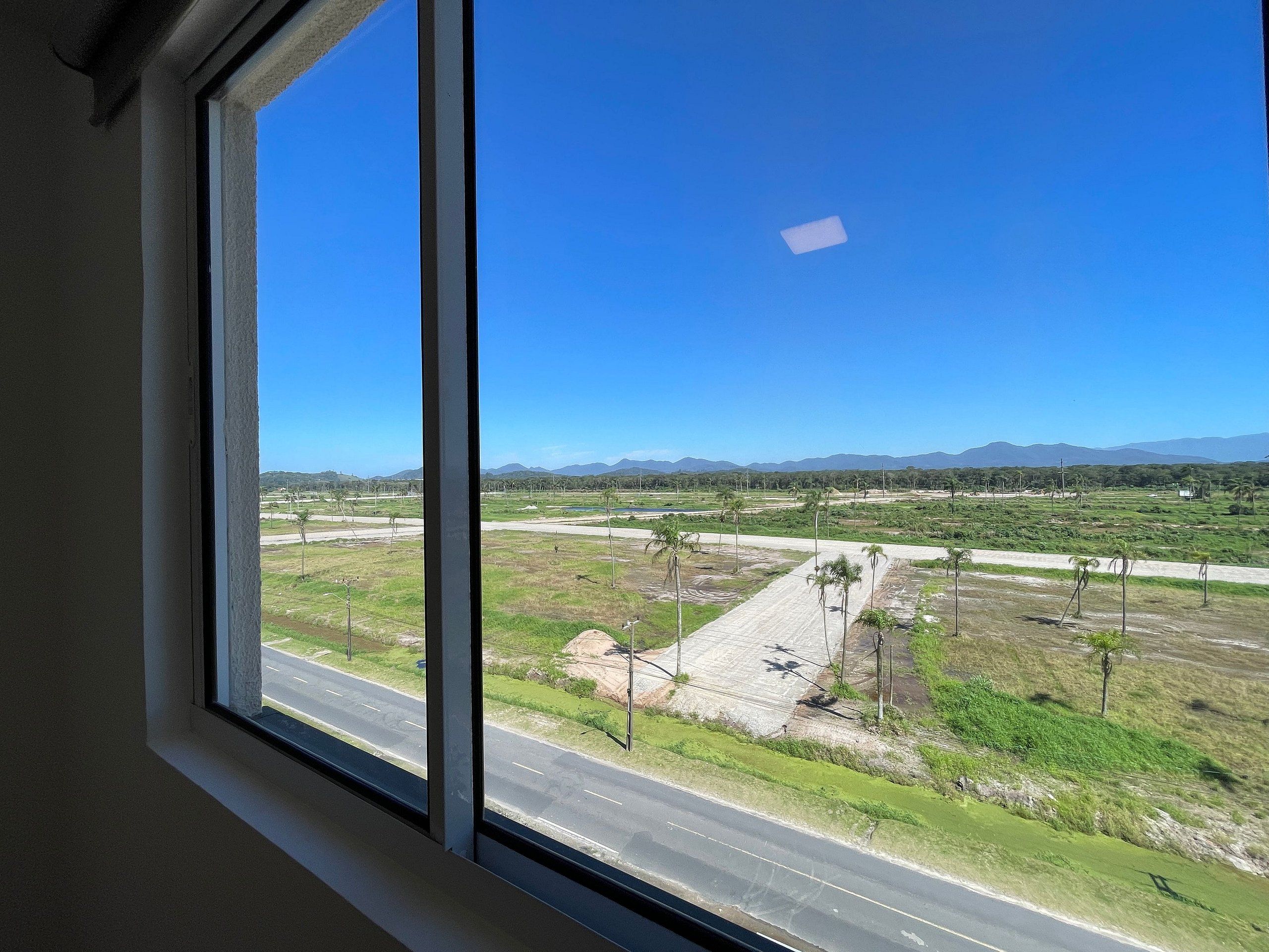 A view through a window of a road with a clear sky, distant mountains, and sparse vegetation.