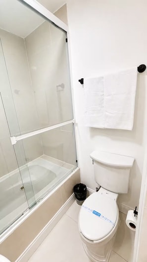 A bathroom with a toilet, a glass-enclosed shower, and a white towel hanging on the wall. - Estudio / StayMty San Agustín. #3 (San Pedro Garza García)