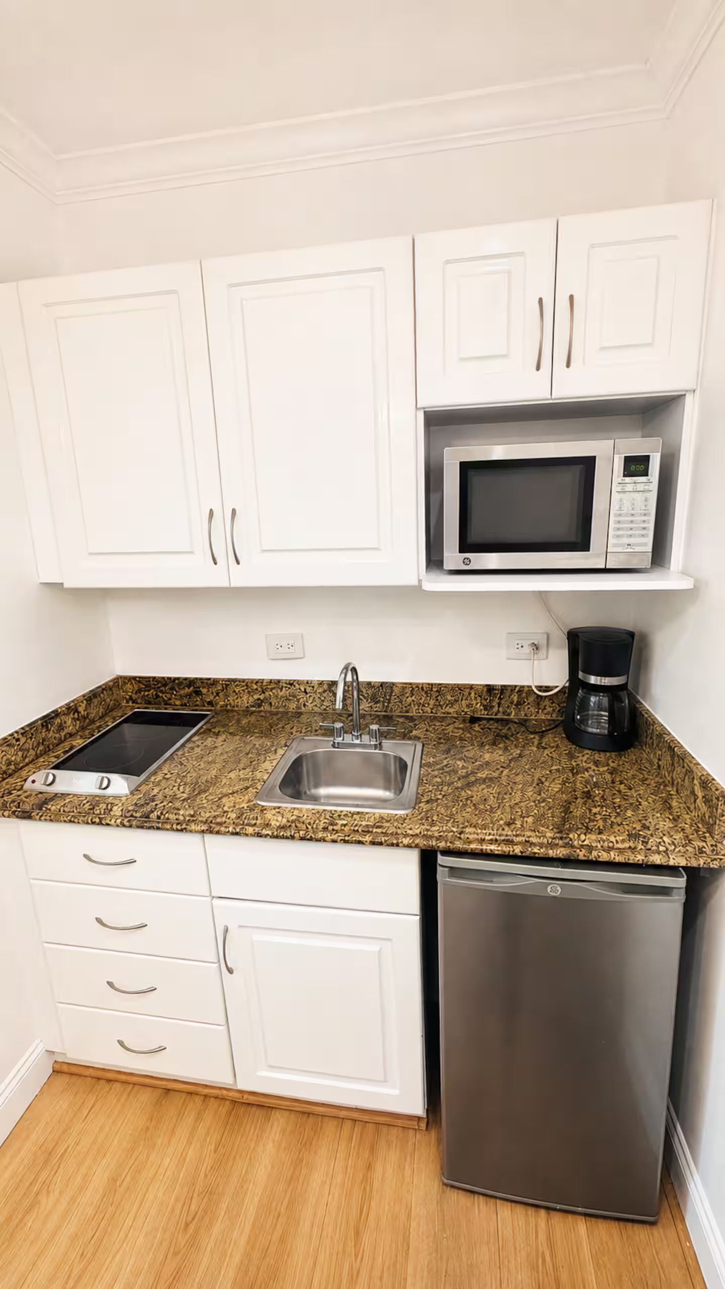 A compact kitchen with white cabinets, a microwave, a coffee maker, a dishwasher, and a gas stove.