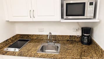 A compact kitchen with white cabinets, a microwave, a coffee maker, a dishwasher, and a gas stove.
