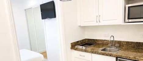 A kitchen with white cabinets, a granite countertop, a stainless steel sink, and a black trash bin.