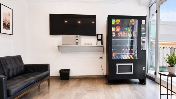 Een moderne woonkamer met een leren bank, een koffieapparaat, een aan de muur bevestigde televisie en een automaat.