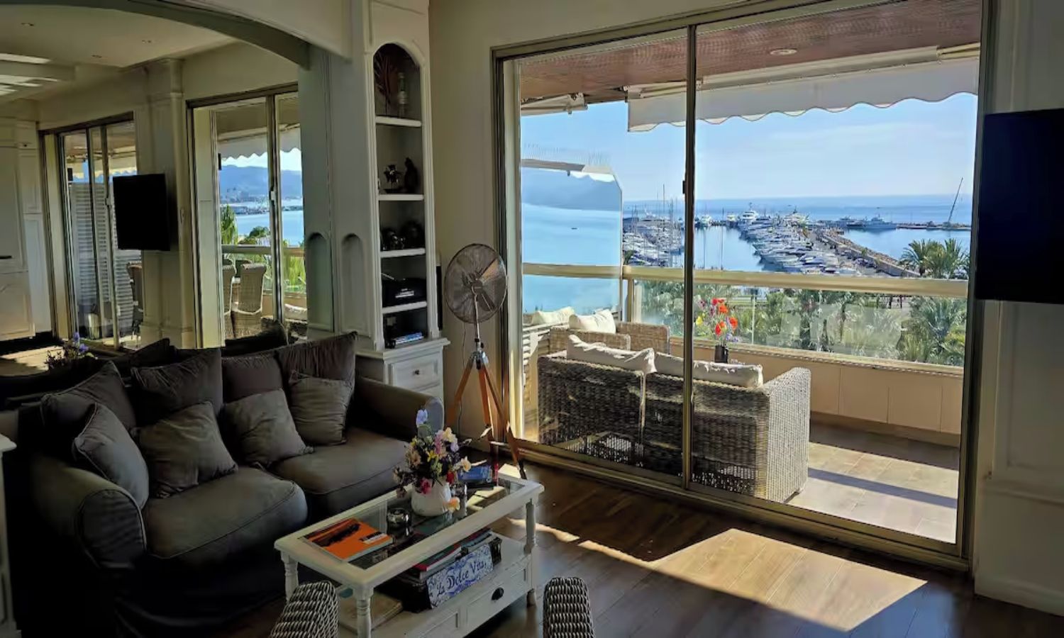 Un salon doté d’une grande porte-fenêtre coulissante donnant sur un balcon avec vue sur un port de plaisance.