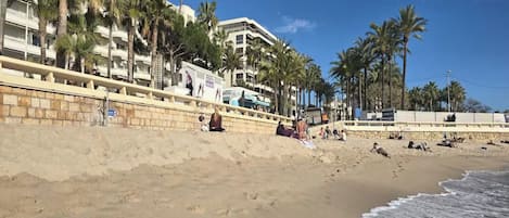 Une plage avec un mur de pierres, des palmiers et un bâtiment doté de balcons.